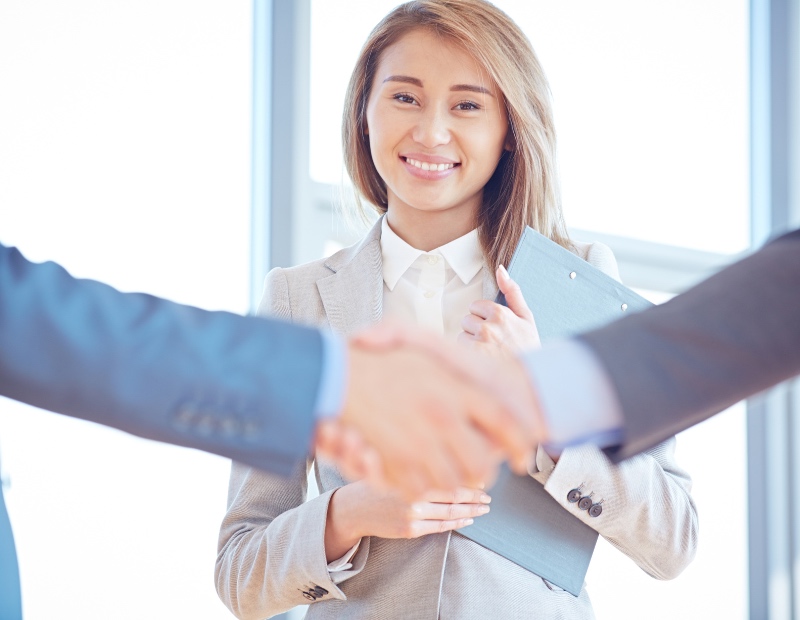 Smiling woman in suit holding a clipboad with shaking hands in foreground